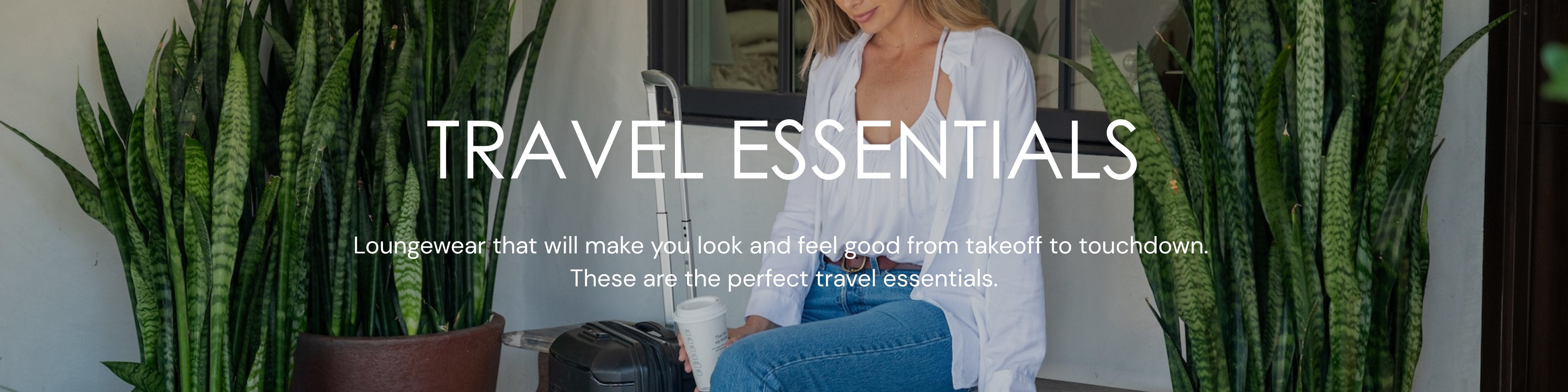 Woman in white Slumber Party Top and jeans sitting outside next to a suitcase.